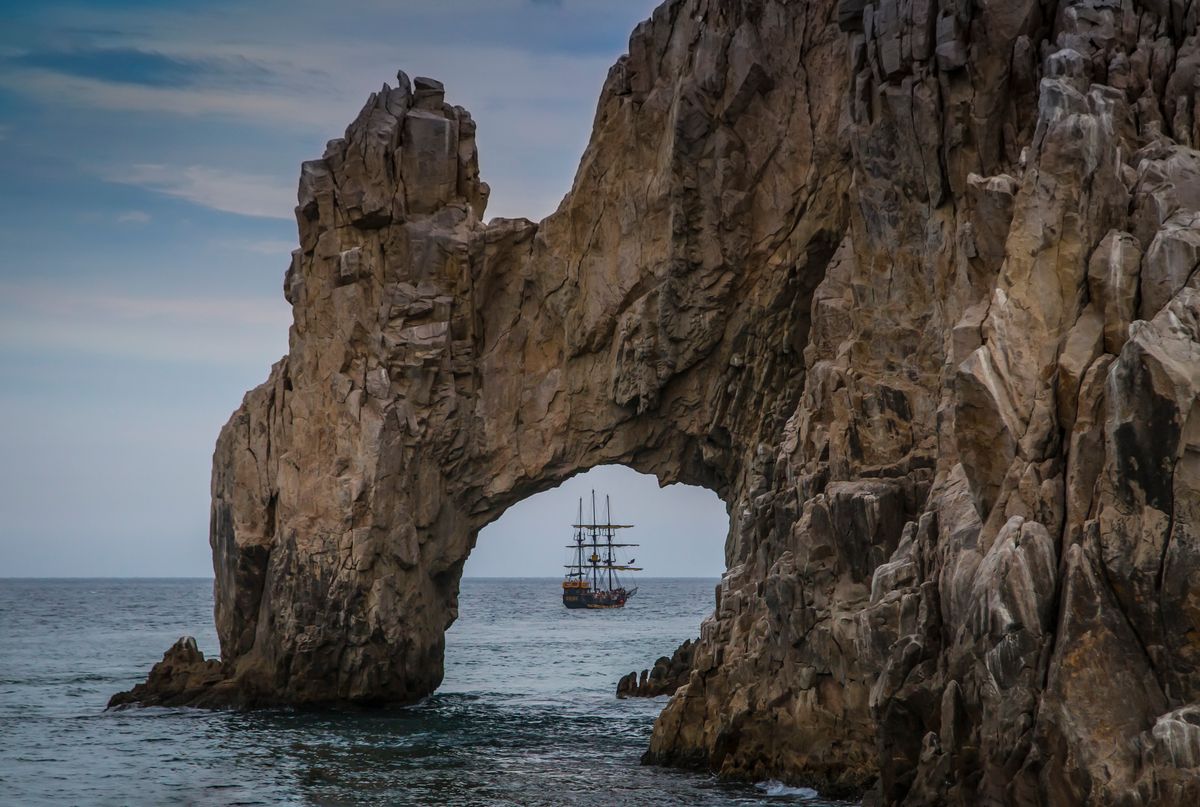 Stunning view of a sailboat passing through a natural rock arch at sea, showcasing nature's wonder.