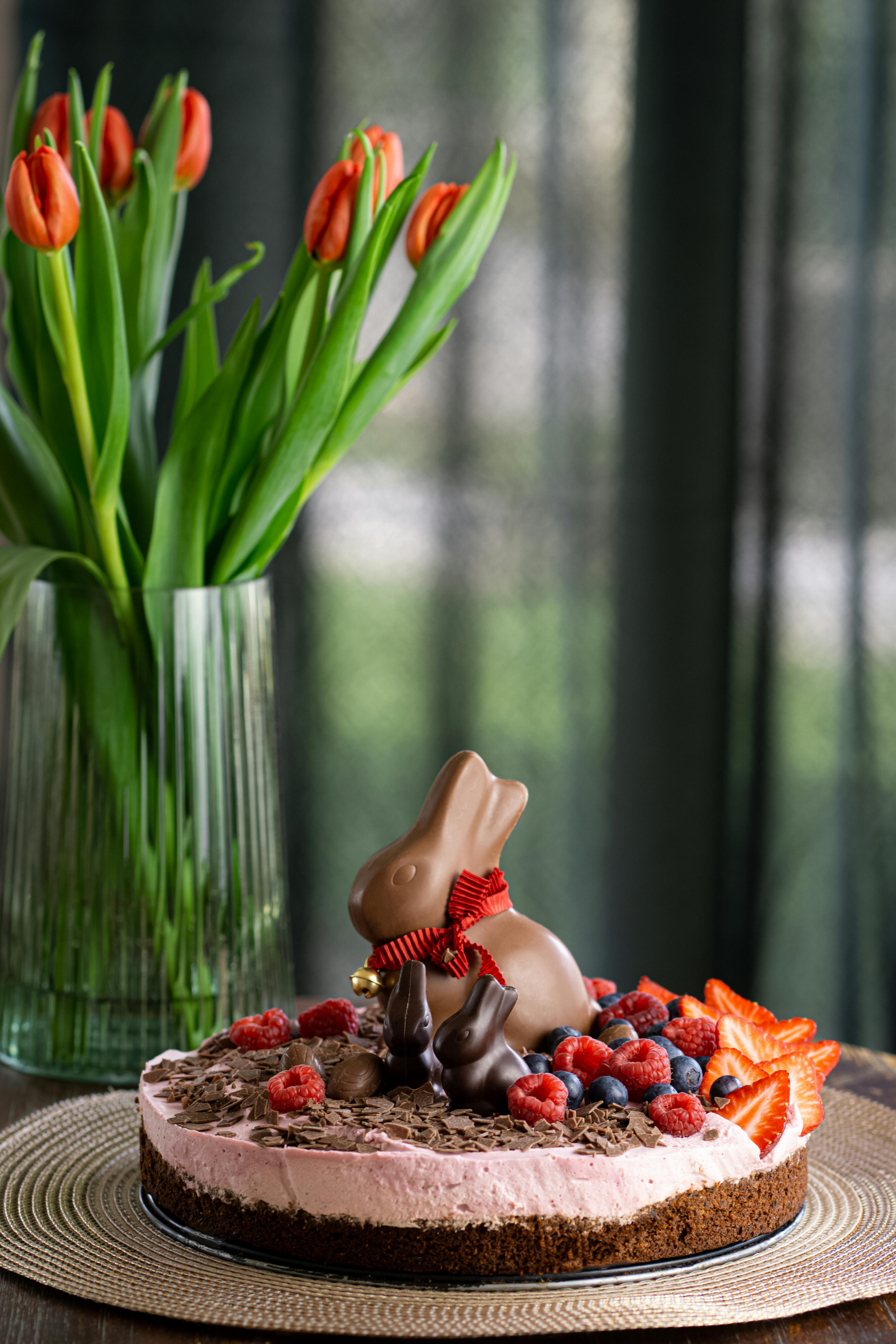 Free Delightful Easter cake topped with a chocolate bunny, berries, and floral decorations. Stock Photo