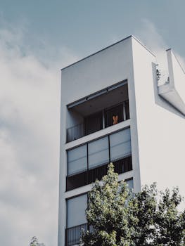 Contemporary apartment facade with balconies and trees on a clear day.