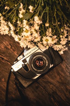 A vintage Praktica camera surrounded by delicate white flowers on a wooden table.