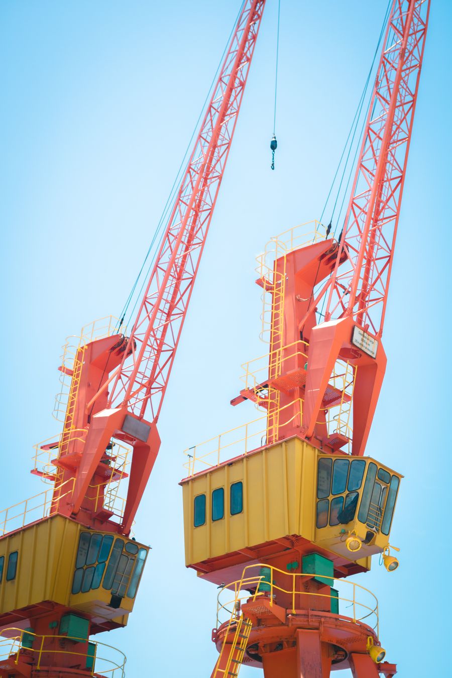 Two red tower cranes against a clear blue sky