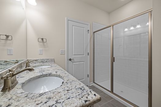 Elegant bathroom featuring granite countertops and a spacious glass shower enclosure.