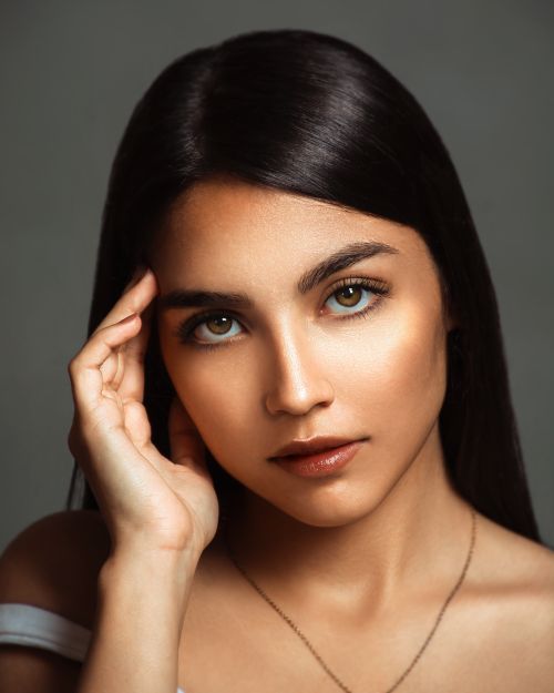 Free Striking portrait of a young woman with dark hair and necklace against a subtle gray background. Stock Photo