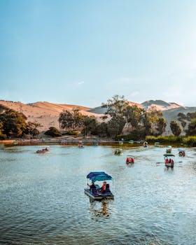 Explore the serene beauty of Huacachina oasis in Peru, featuring boats on tranquil water surrounded by desert dunes.