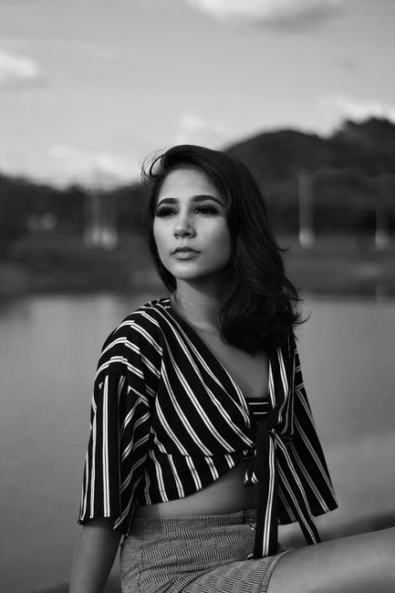 Black and white portrait of a woman in a striped dress by a serene lake.