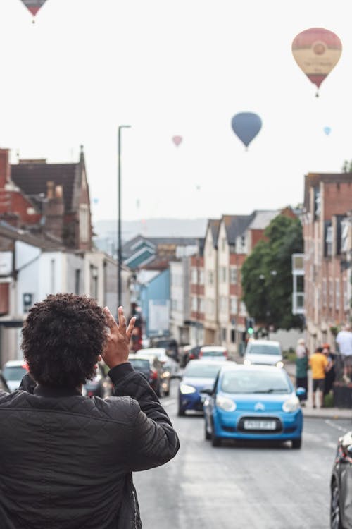 Man Taking Photo of Hot Air Balloons Flying over City