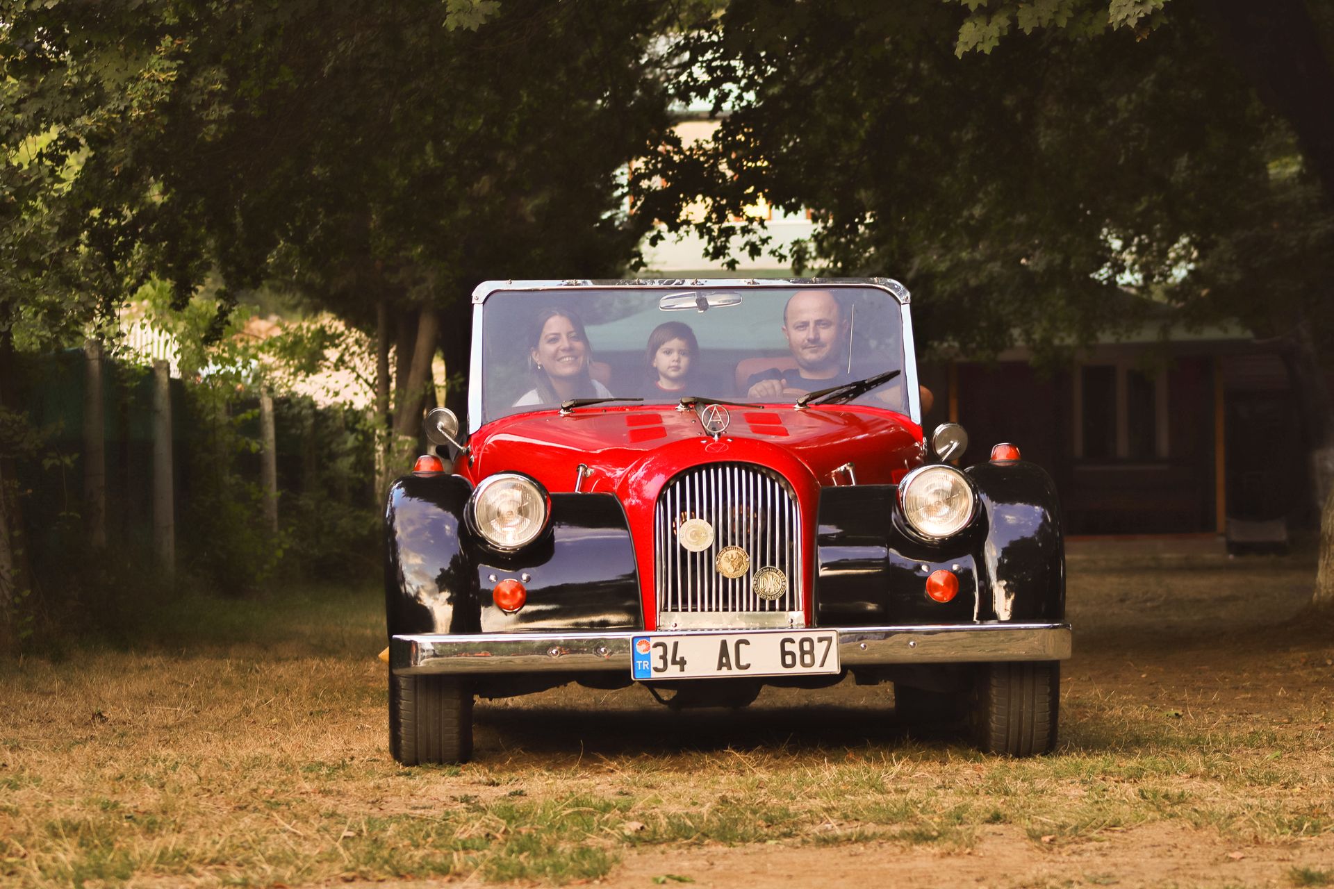 Happy family driving a classic vintage car in a rural setting, enjoying a sunny day outdoors.