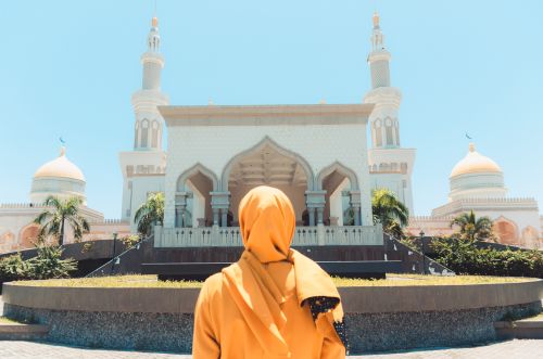 Free A woman in an orange headscarf looks at a beautiful mosque on a sunny day. Stock Photo