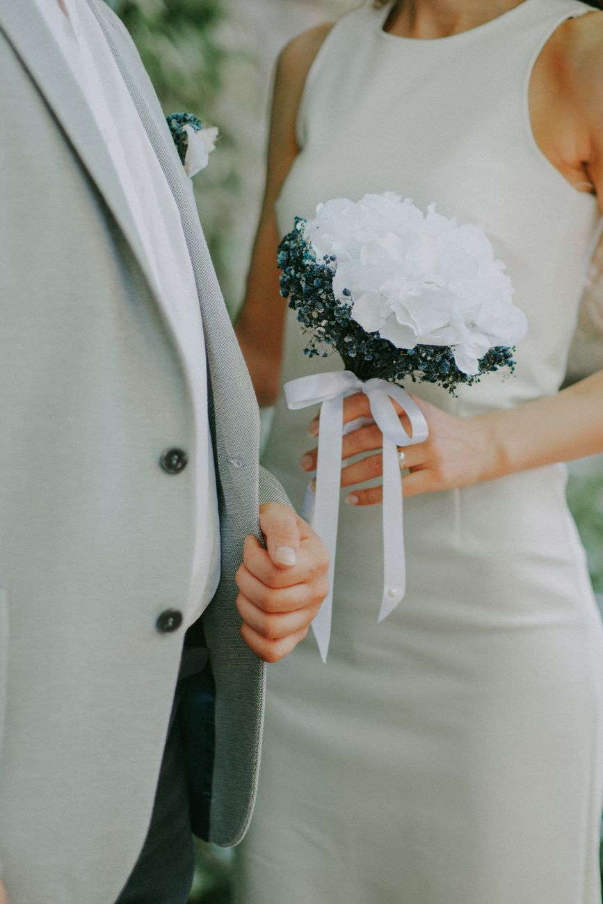 A wedding couple dressed elegantly with focus on the bride holding a white floral bouquet.