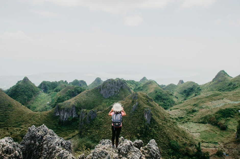 A woman with a backpack overlooks rolling green hills on a clear day.