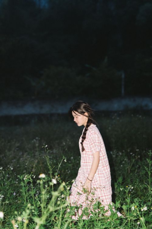 Free A young woman in a plaid dress strolls through a meadow at night, creating a serene fashion scene. Stock Photo
