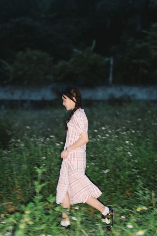 Free A woman in a dress walks through a meadow at night, surrounded by plants. Stock Photo
