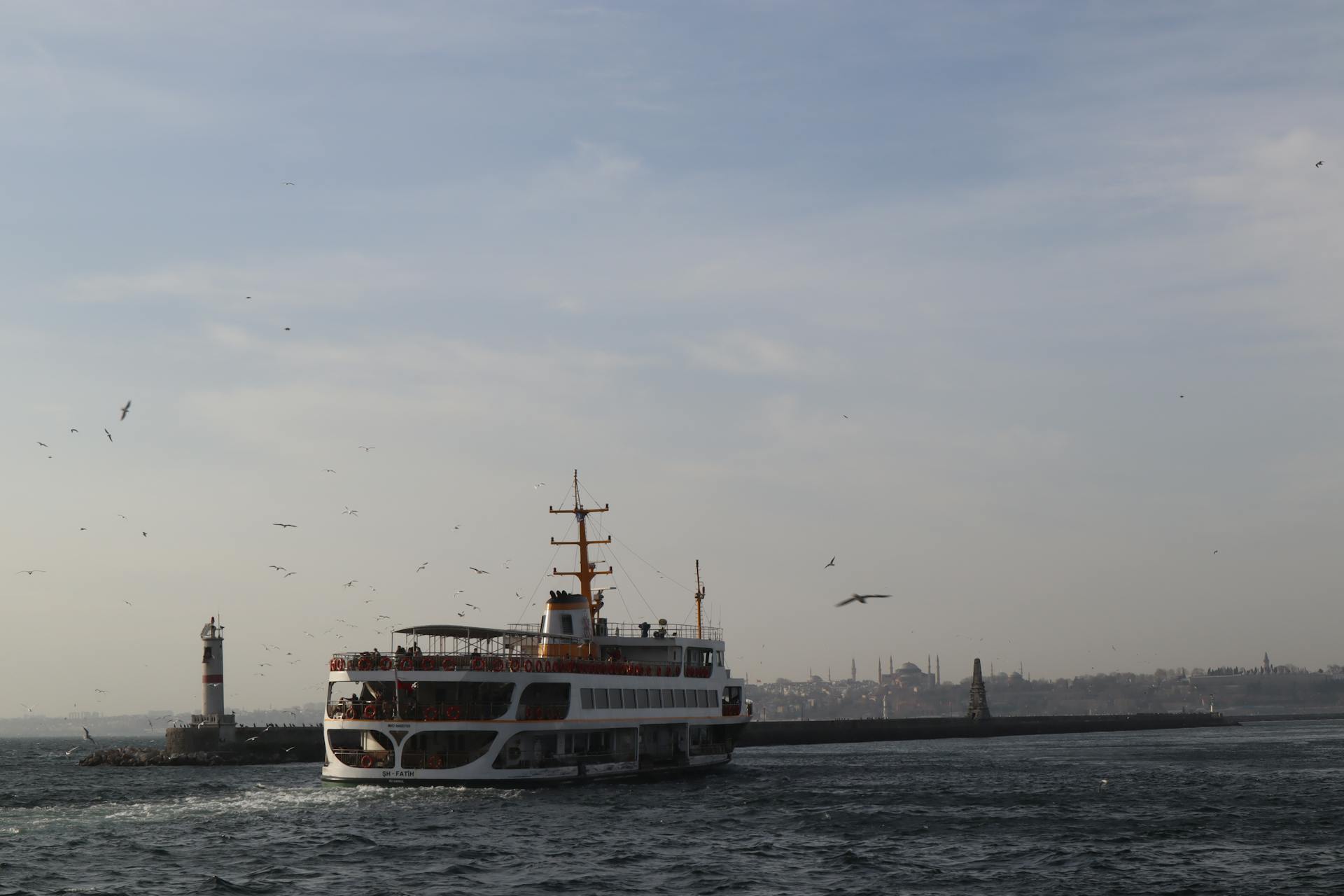 Ferry ship cruising near a lighthouse with skyline in the background, ideal for travel themes.