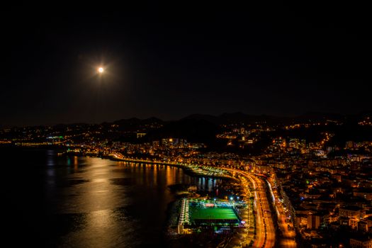 Aerial night cityscape of Giresun, Türkiye with illuminated coastline and moonlight.