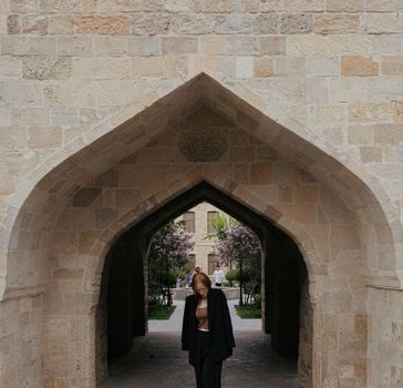 Woman in dark clothing walks through a stone archway in Baku, Azerbaijan.