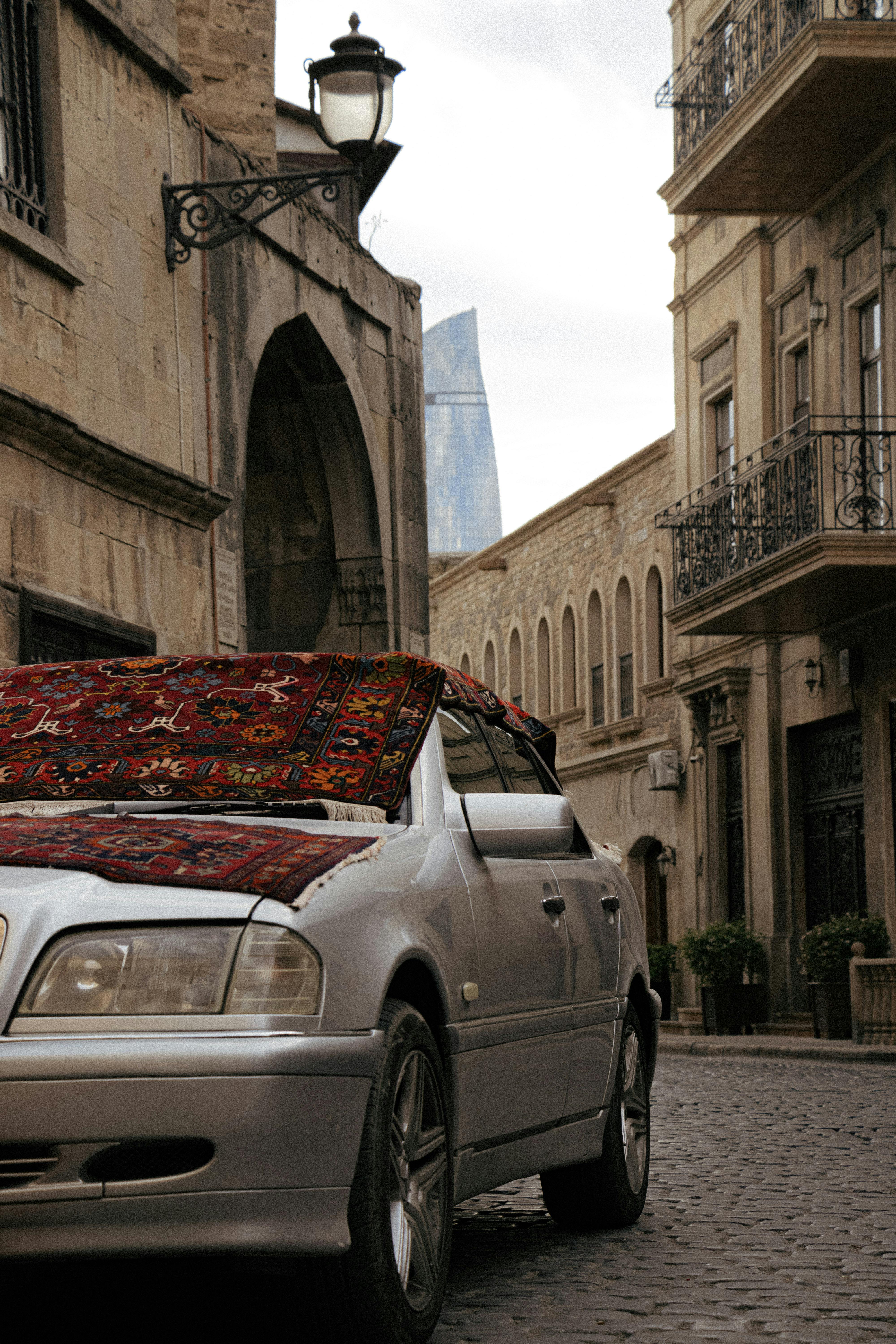 Silver car with traditional carpet in Baku's historic Old Town street.