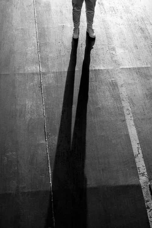Free Black and white photo showing a long shadow cast by a standing person on concrete pavement. Stock Photo