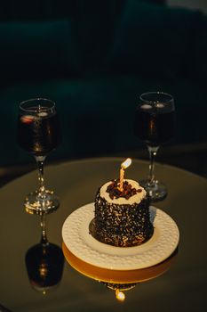 A lavish setup featuring a chocolate cake with a lit candle and two glasses of red wine, perfect for a special occasion.