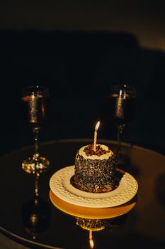 A dark and intimate setting featuring a chocolate cake with a lit candle, flanked by two glasses of wine.