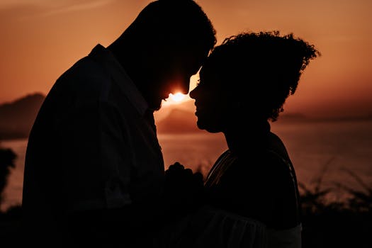 A couple shares an intimate moment in silhouette against a stunning sunset backdrop.