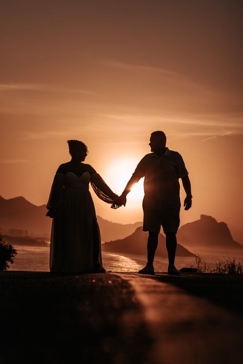Free Silhouette of a couple holding hands at sunset near a coastline, capturing love and nature's beauty. Stock Photo