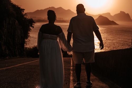 Free A couple walking hand in hand at sunset on a scenic coastal path, silhouetted against the sea. Stock Photo