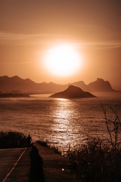 Free Dramatic sunset over ocean with silhouetted hills, casting a golden glow on the water. Stock Photo