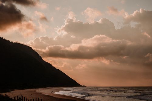 Free Tranquil beach at sunset with dramatic clouds and mountain silhouette. Stock Photo