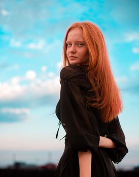 A young redhead woman in a black dress poses gracefully outdoors in Baku, Azerbaijan.