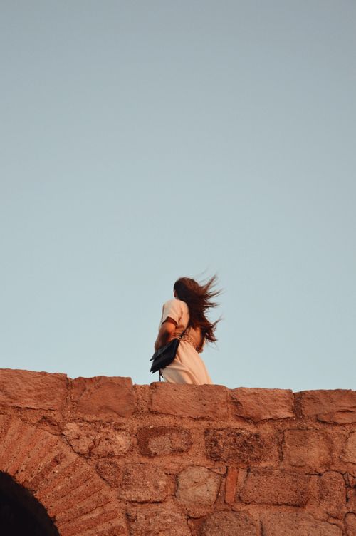 Free A woman with flowing hair walking along an ancient stone wall under a bright clear sky in Ankara. Stock Photo