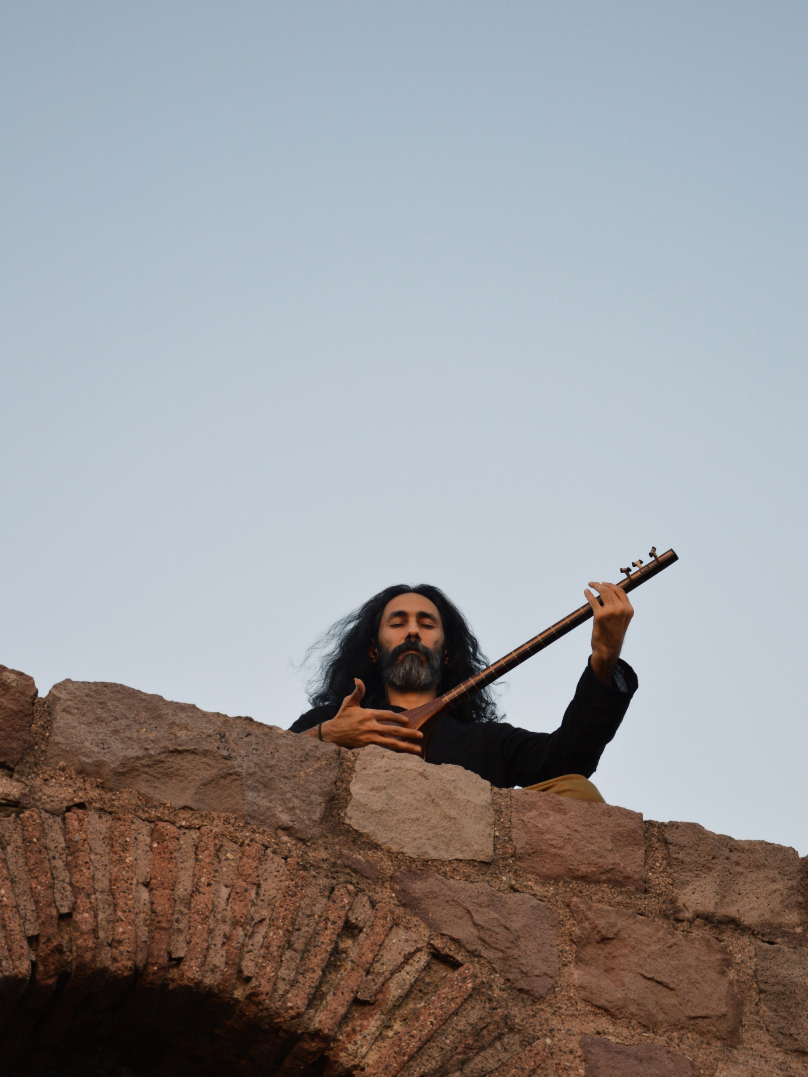 Man performing on a saz instrument atop a stone wall in Ankara, Türkiye.