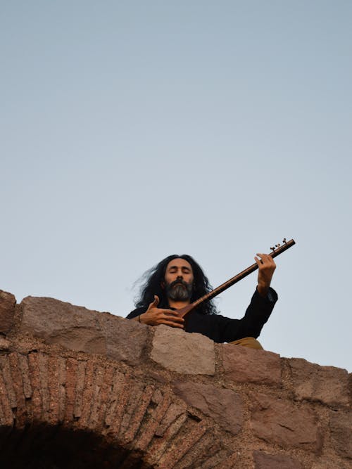 Man Standing atop Stone Wall Playing Instrument