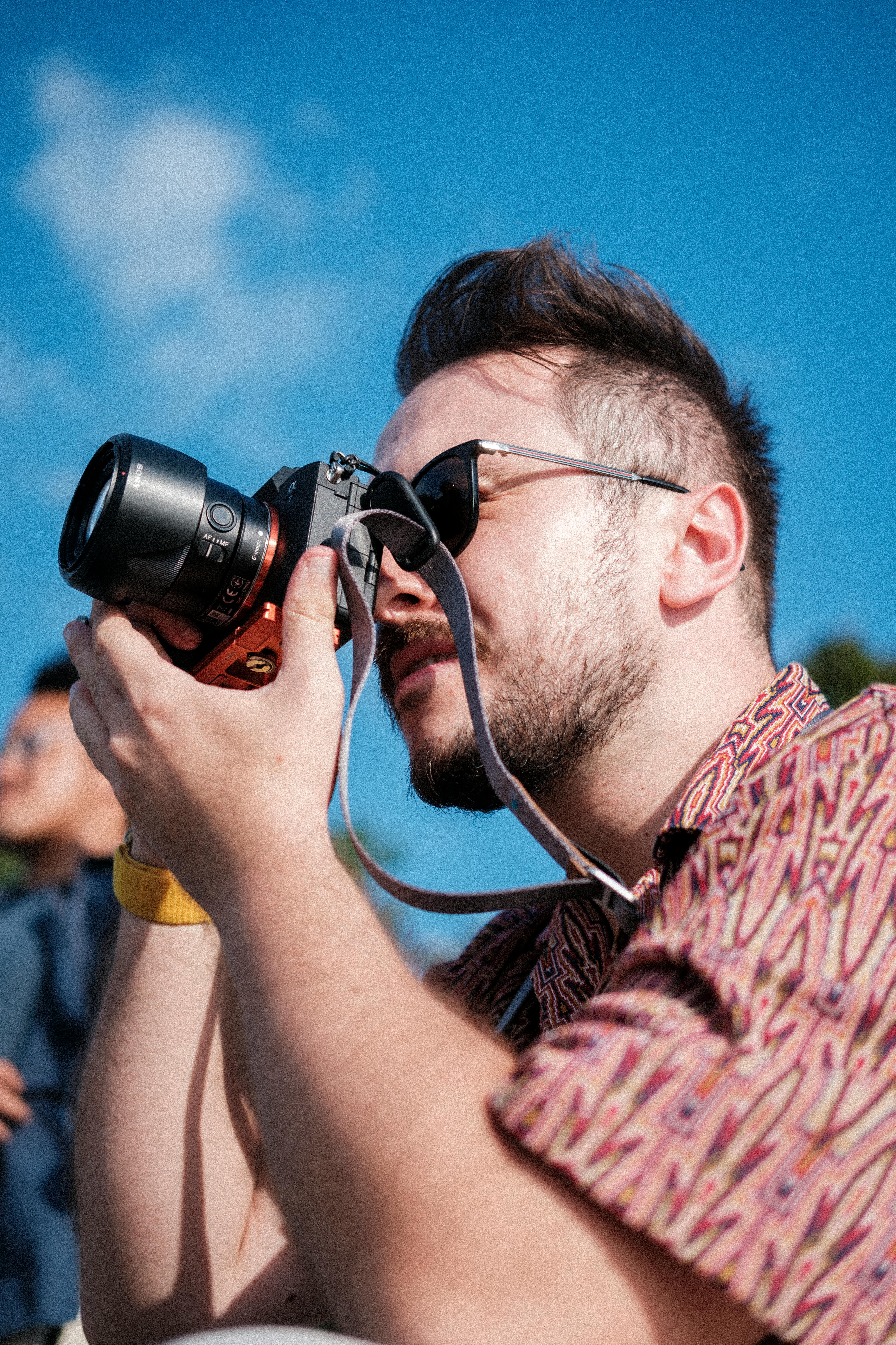 Free Photographer capturing a scene outdoors with a camera under a bright blue sky. Stock Photo