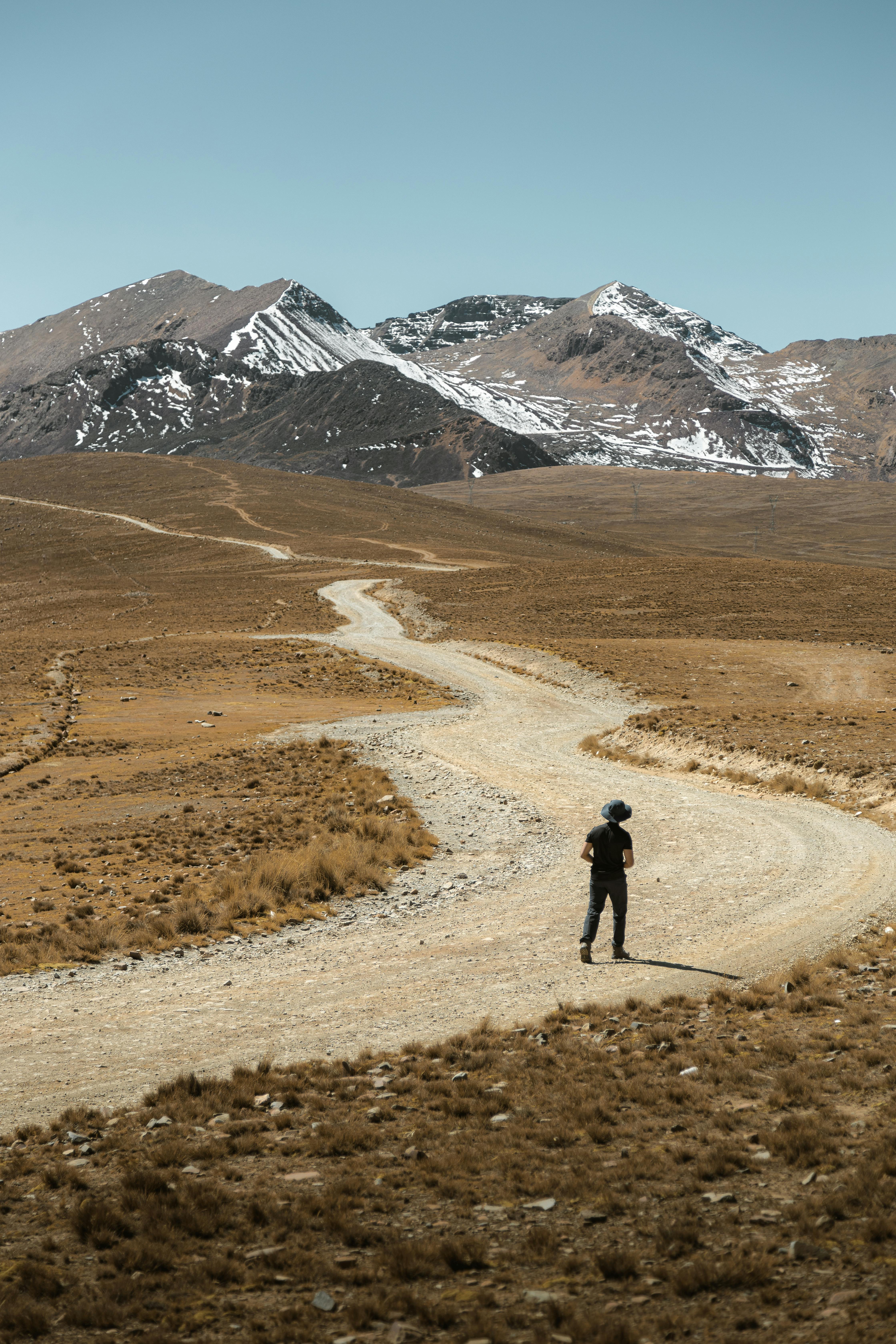 A lone traveler walking on a winding road through a mountainous desert landscape.