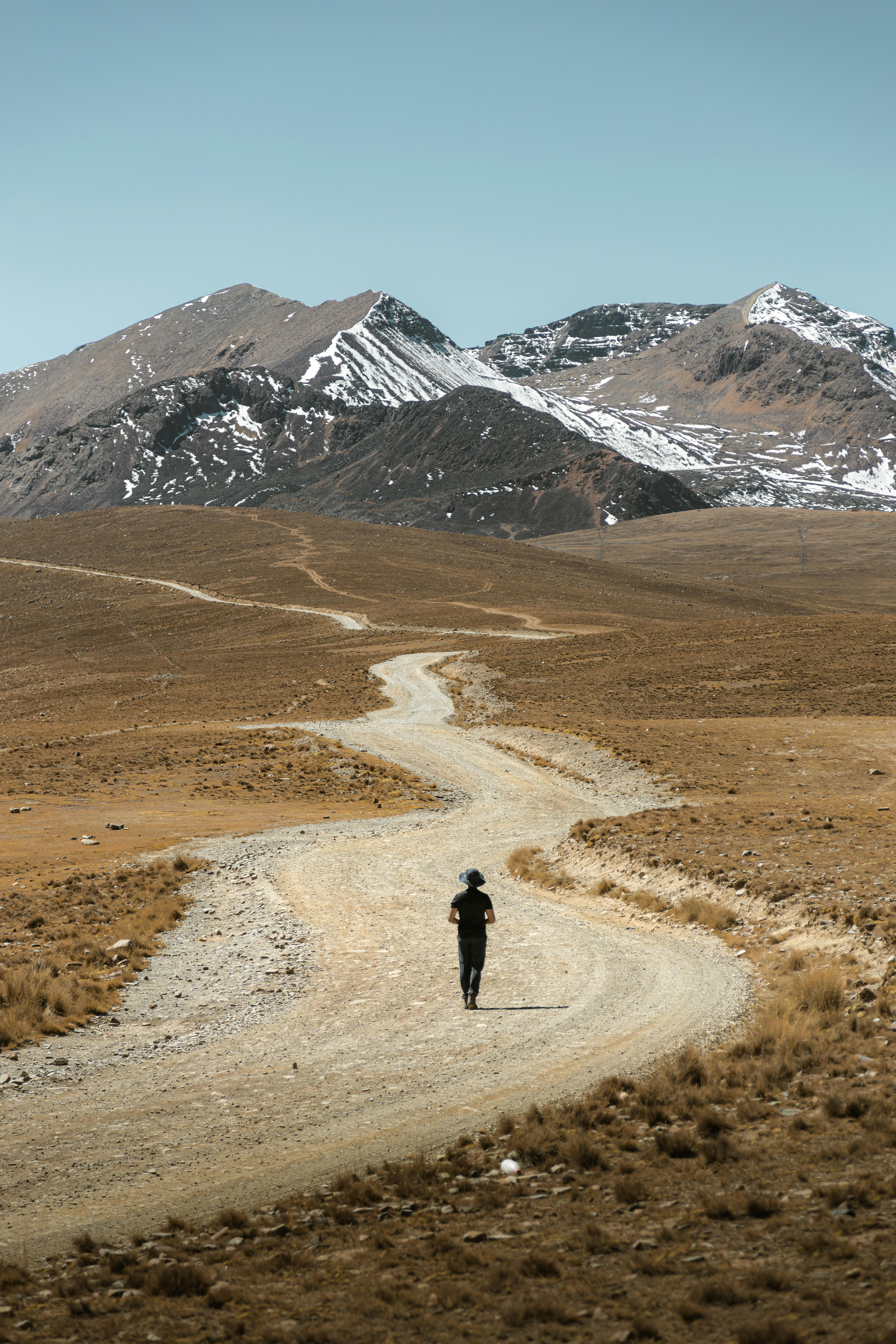 A solitary figure walks on a winding road through barren mountain landscape, evoking a sense of adventure.
