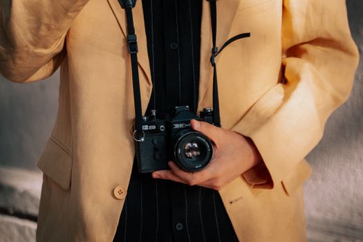 Person holding a vintage camera, dressed in a stylish coat outdoors.