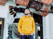 一位穿着黄色连帽衫的时尚男子，在户外自信地摆着姿势，充满活力