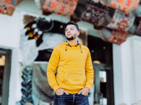 一位穿着黄色连帽衫的时尚男子，在户外自信地摆着姿势，充满活力