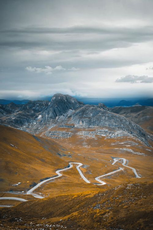 Free A breathtaking view of winding roads through stunning mountain landscapes under cloudy skies. Stock Photo