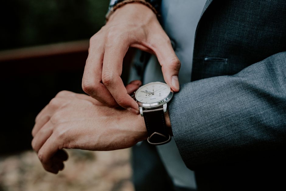 Close-up of a man adjusting his wristwatch, wearing a formal suit, outdoors during the day.