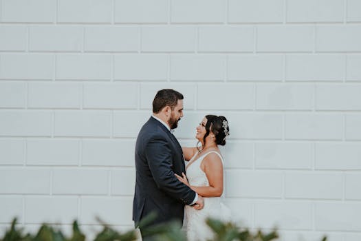 A joyful newlywed couple embracing against a white brick wall, capturing a candid moment of love.