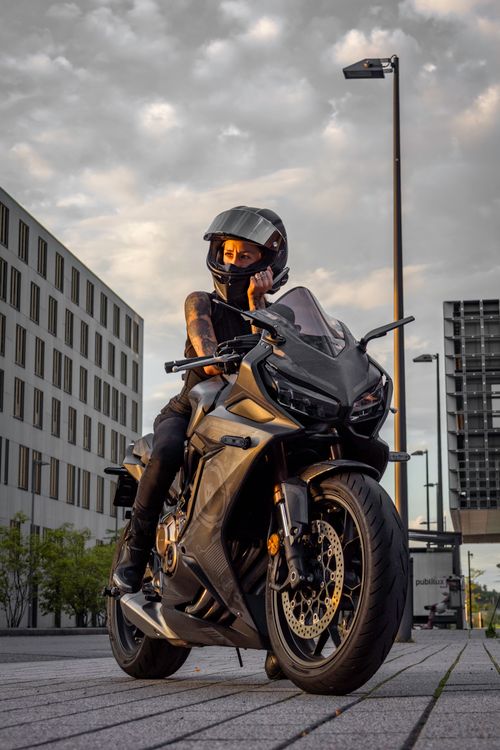 Free Woman on a motorcycle in an urban setting at sunset, capturing a modern and rebellious vibe. Stock Photo