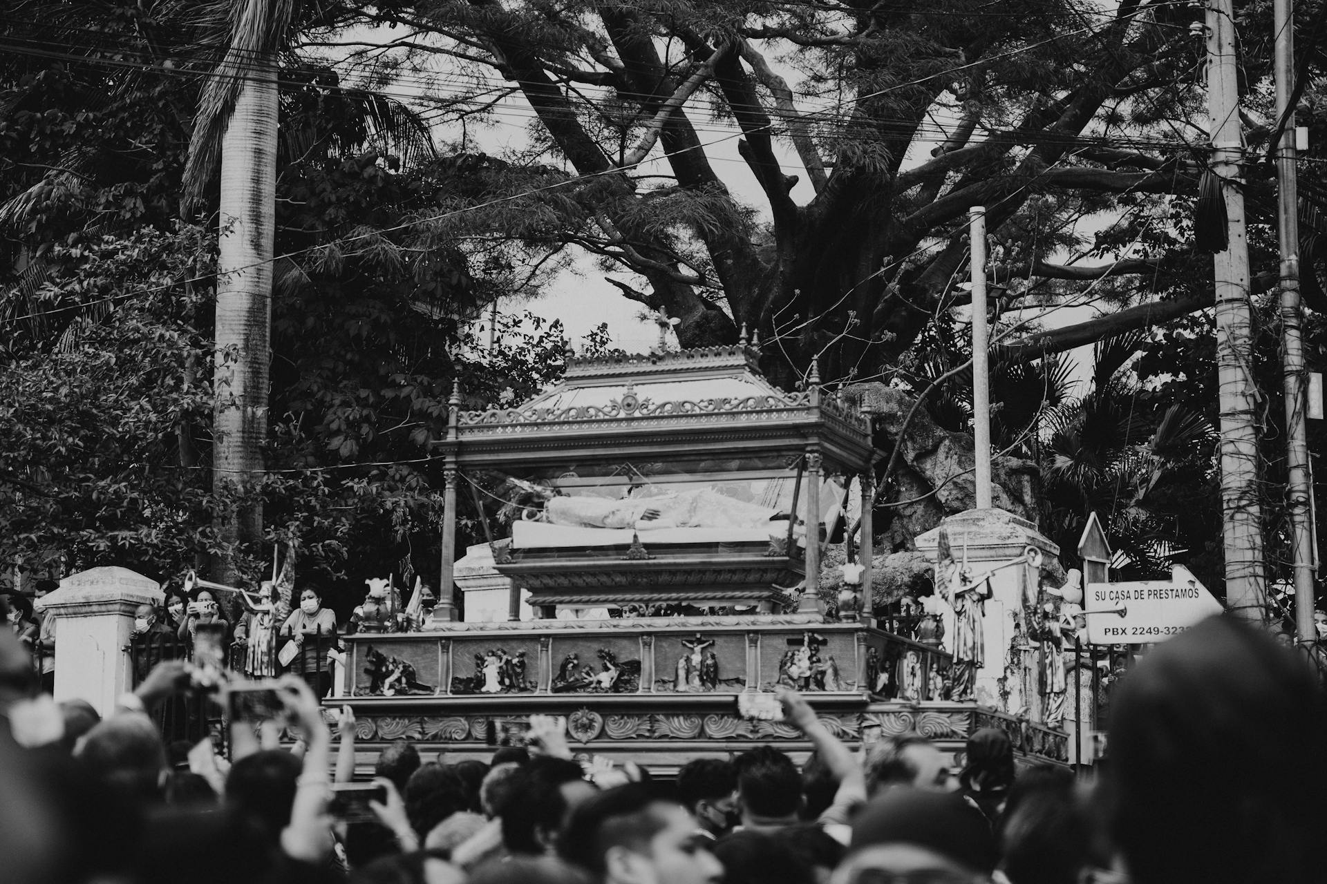 A somber black and white photograph capturing a religious funeral procession with a catafalque.