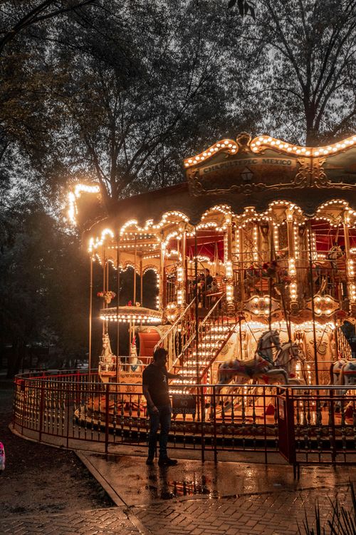 Free A magical evening view of a brightly lit carousel in a park with a silhouette of a man. Stock Photo