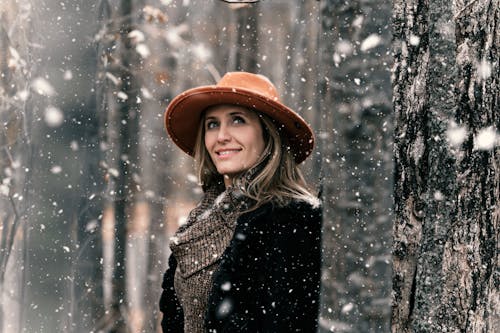 Smiling Woman Standing Near Tree With Snow Falling