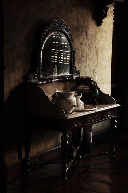 Antique wooden vanity with mirror and decorative pottery, creating a moody vintage interior scene.