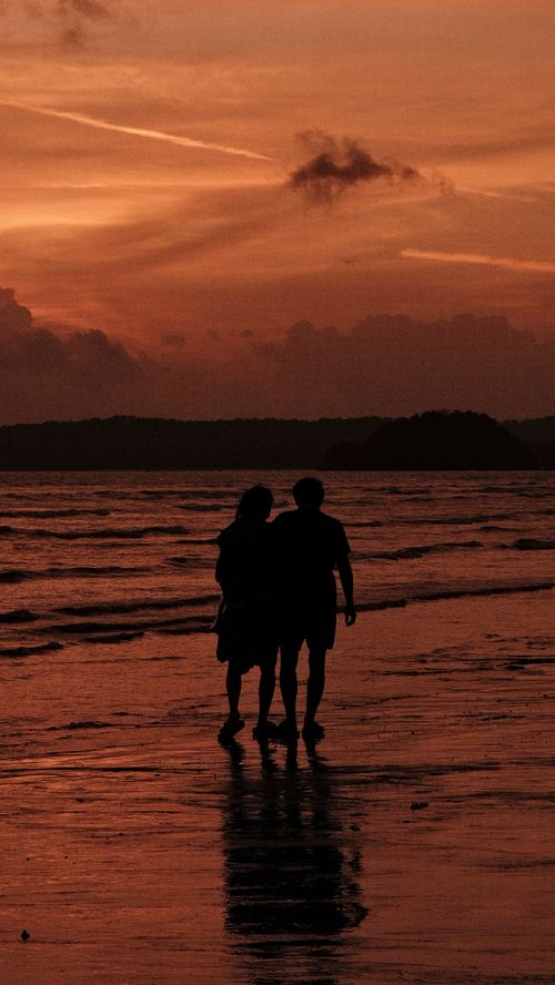 Free Silhouette of a couple walking along the beach during sunset, capturing a romantic and serene moment. Stock Photo
