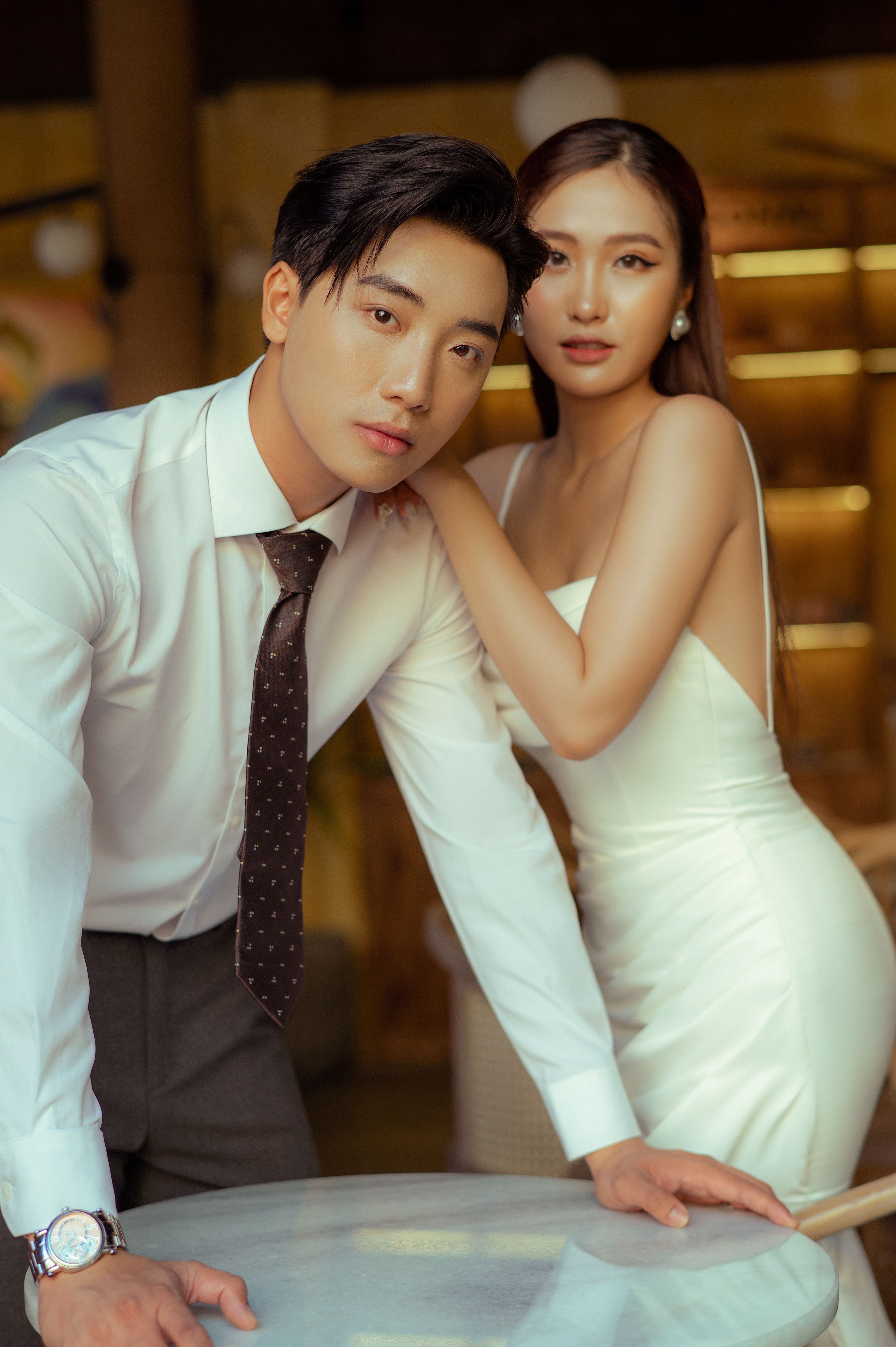 Stylish Asian couple elegantly posing indoors against a warm background, exuding sophistication.