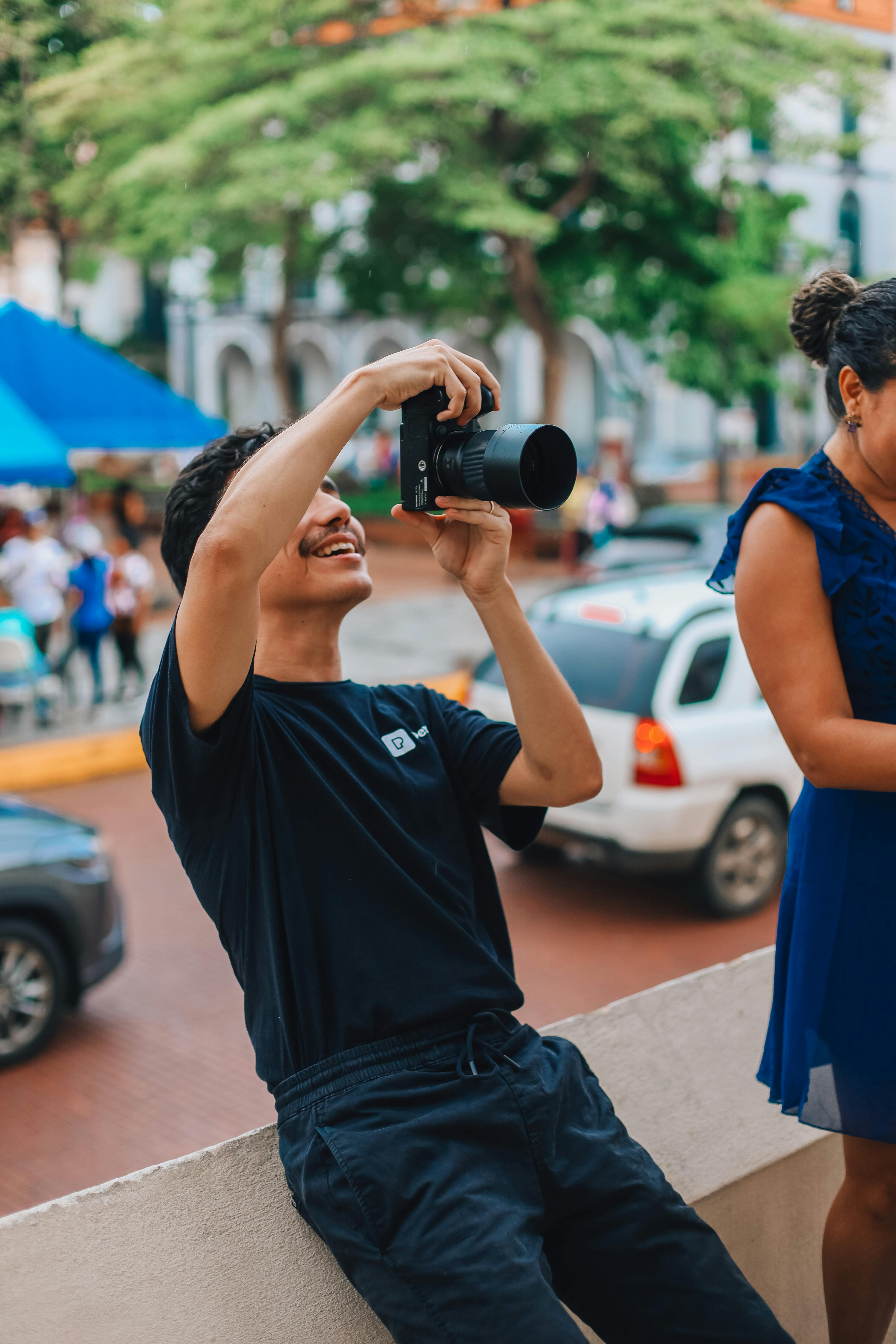 Smiling young man with camera taking photos in a vibrant city street scene.