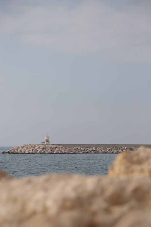 Free A serene coastal scene with a lighthouse on a rocky shore under a clear sky, ideal for backgrounds. Stock Photo